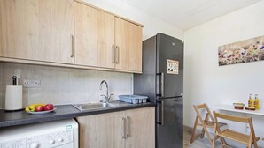 Una cocina compacta con muebles de madera, un refrigerador de acero inoxidable, una lavadora y un lavamanos.