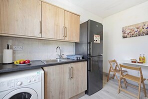 Ett kompakt kök med träskåp, ett kylskåp i rostfritt stål, en tvättmaskin och ett handfat.