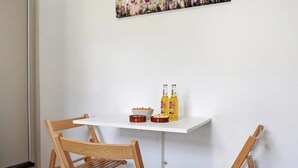 Un pequeño comedor con dos sillas de madera, una mesa blanca y un cuadro en la pared.