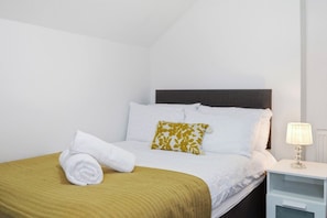 A hotel room with a bed, a nightstand, and a lamp.