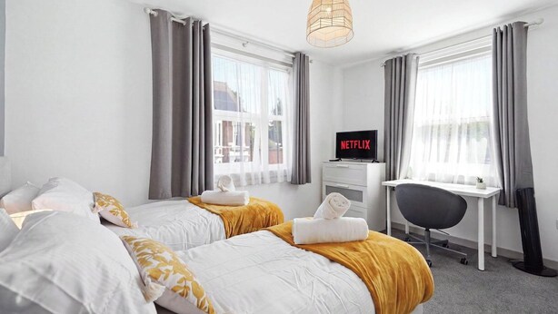 Habitación de hotel con dos camas, un escritorio, una silla, un televisor y una lámpara colgante.