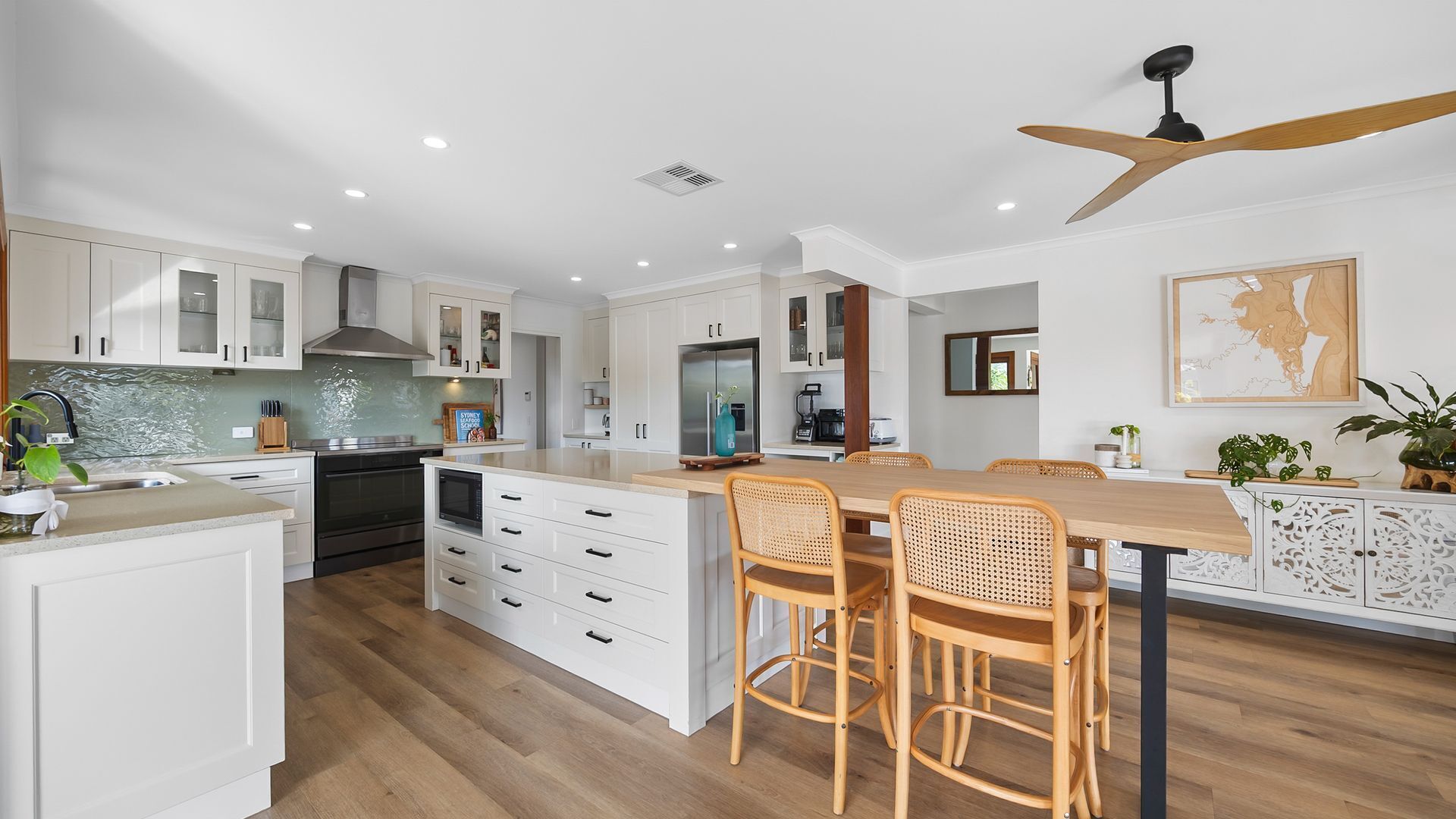A modern kitchen with white cabinetry, a central island with seating, and a ceiling fan.