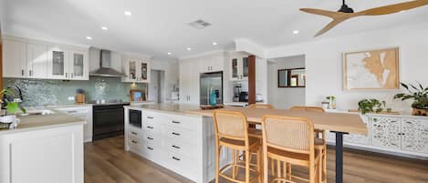 A modern kitchen with white cabinetry, a central island with seating, and a ceiling fan.