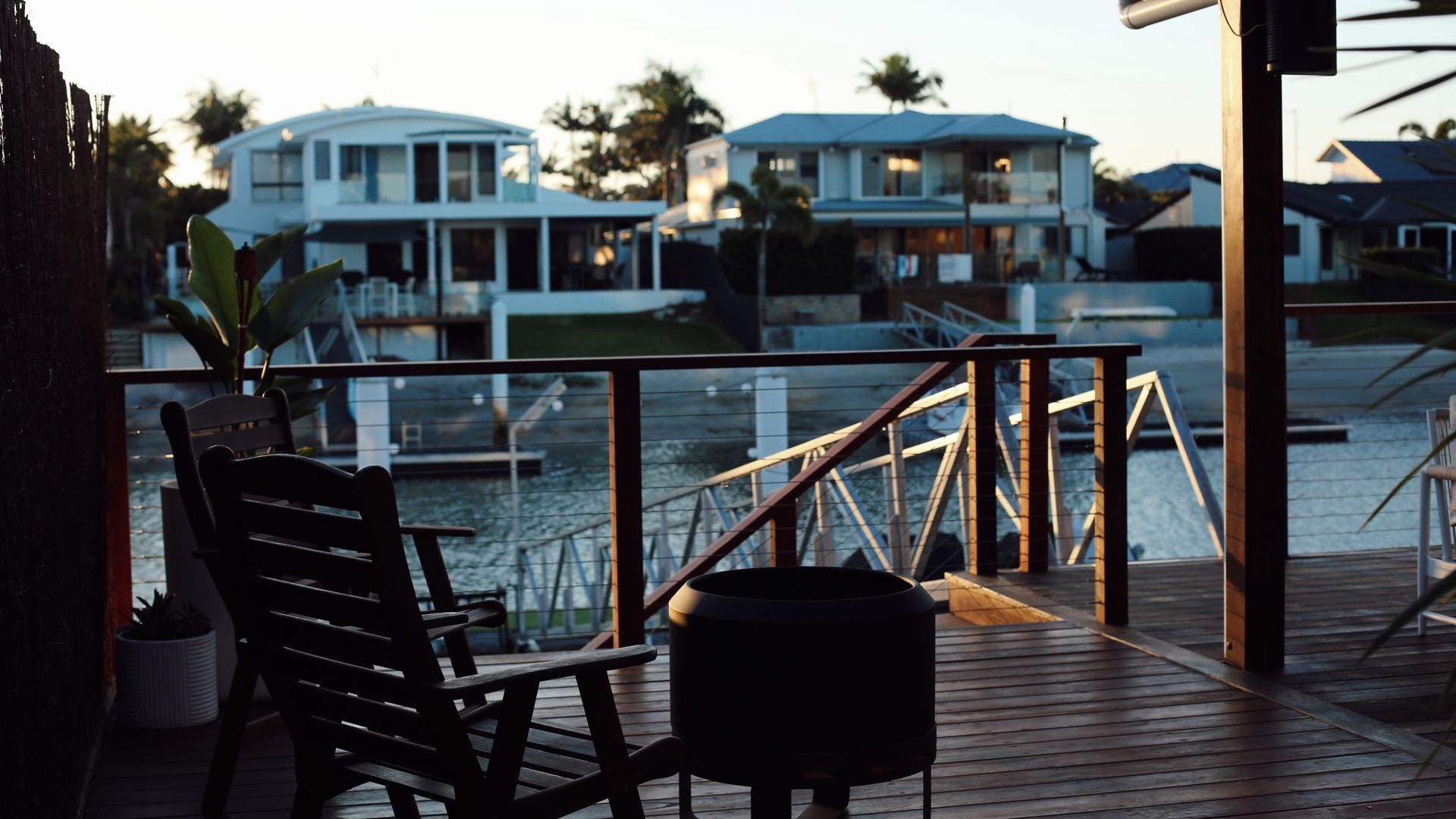 A wooden deck with a chair and a small table, overlooking a marina with boats and houses in the background.