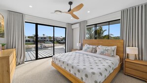 A bedroom with a large bed, a ceiling fan, a nightstand, a lamp, and a view of the outside. - Waterfront Retreat in the heart of Mooloolaba (mooloolaba)