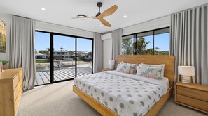 A bedroom with a large bed, a ceiling fan, a nightstand, a lamp, and a view of the outside. - Waterfront Retreat in the heart of Mooloolaba (mooloolaba)