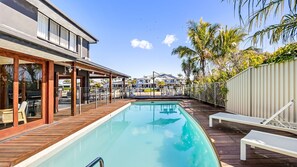 A swimming pool with a wooden deck, lounge chairs, and a view of other buildings in the background. - Waterfront Retreat in the heart of Mooloolaba (mooloolaba)