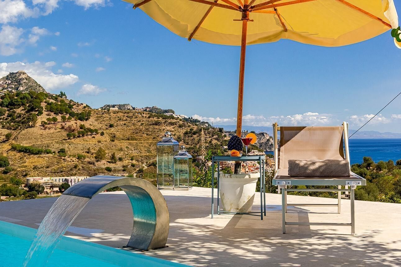 A poolside area with a chair, umbrella, and a table with a drink.