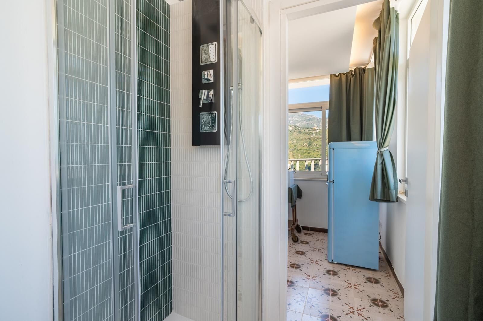 Ein Badezimmer mit Dusche, Toilette und Waschbecken. Ein Fenster mit Vorhängen bietet einen Blick ins Freie.