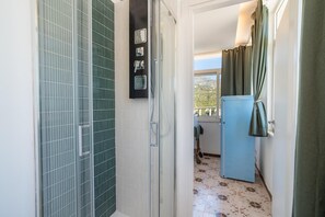 A bathroom with a shower, a toilet, and a sink. There is a window with curtains and a view of the outside. - Casa Musica: Villa Suite with Panoramic Pool (Giardini Naxos)