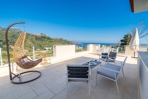 A terrace with a hanging chair, a table with chairs, and a view of the sea. - Casa Musica: Villa Suite with Panoramic Pool (Giardini Naxos)