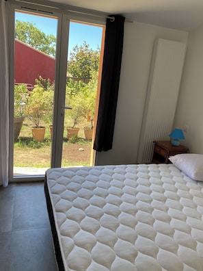 A bedroom with a bed, a nightstand, a lamp, and a view of a garden through a sliding door. - Family home in La Digue for 8 people on the Jade Coast (La Bernerie-en-Retz)