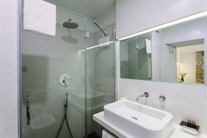 Ein modernes Badezimmer mit einer Duschkabine aus Glas, einem weißen Waschbecken und einem Spiegel darüber.