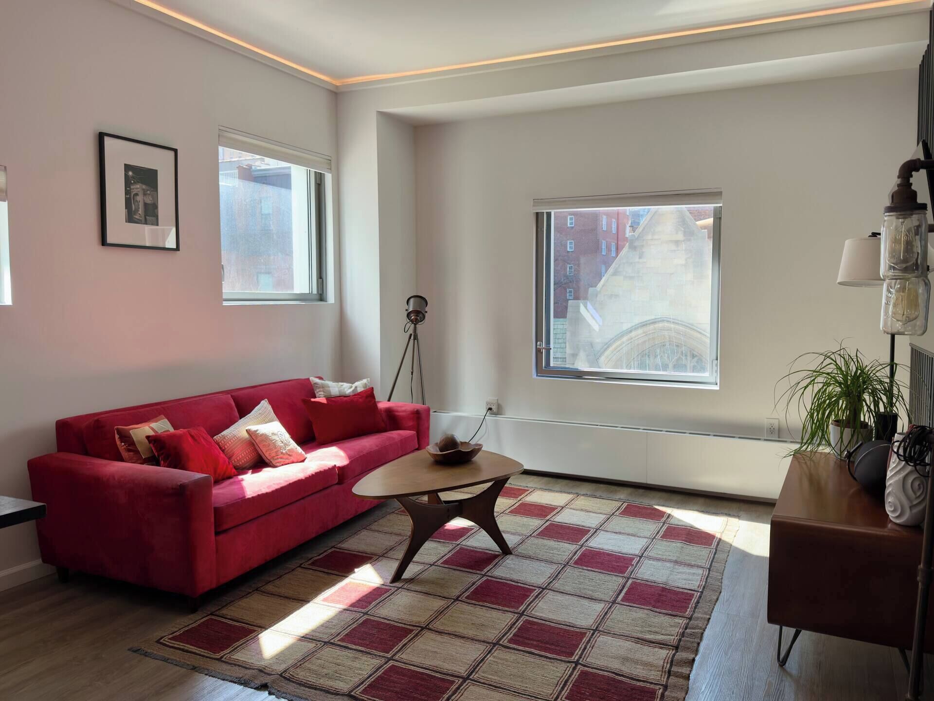 A modern living room with a red sofa, a coffee table, and a view of a building through large windows.
