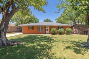 Een gelijkvloers bakstenen huis met een voordeur, een klein portaal en een gazon.