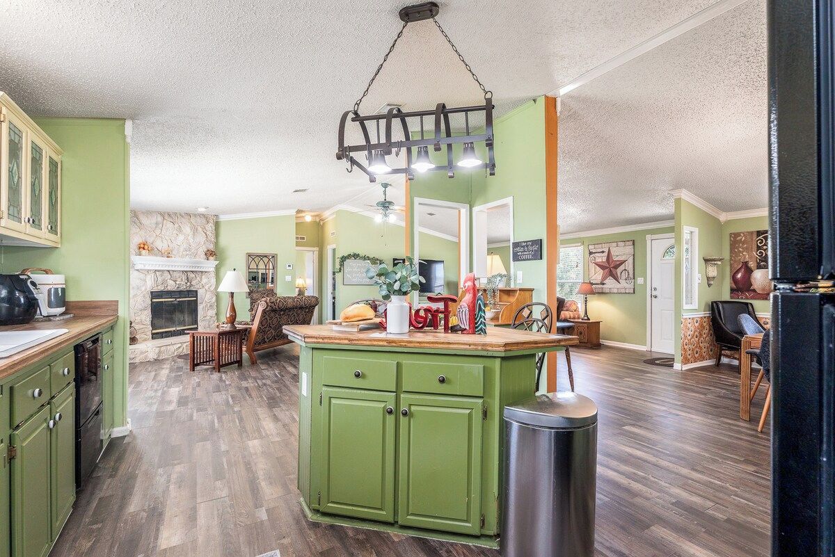 A kitchen with green cabinets, a wooden countertop, and a hanging light fixture.