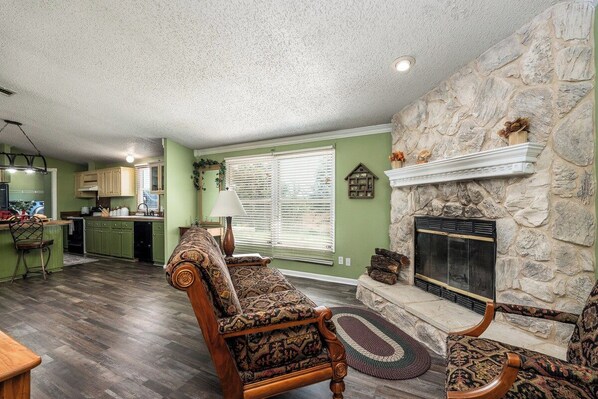A living room with a stone fireplace, a patterned sofa, and a kitchen in the background.