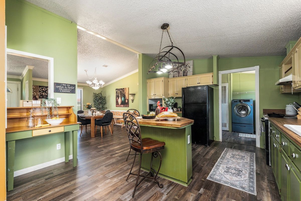 A kitchen with green walls, wooden countertops, a central island, a chandelier, and a washing machine.