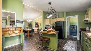 A kitchen with green walls, wooden countertops, a central island, a chandelier, and a washing machine.