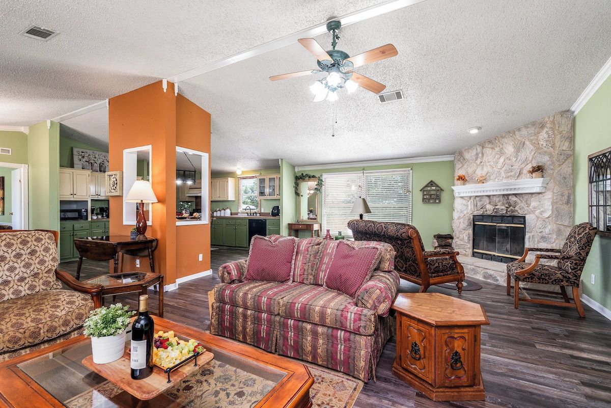 A living room with a sofa, chairs, a fireplace, and a kitchen in the background.