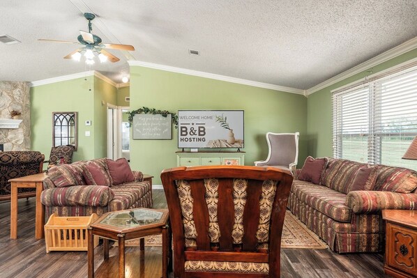 A living room with two patterned sofas, a wooden chair, a glass coffee table, and a ceiling fan.