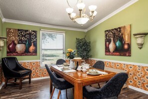 A dining room with a wooden table and chairs, a chandelier, and artwork on the walls.