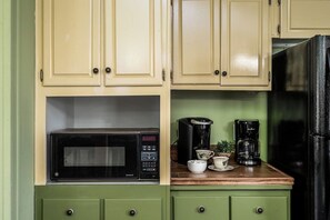 A kitchen with green cabinets, a black microwave, a coffee maker, and a black refrigerator.