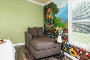 A room with a green wall, a brown sofa, a window with blinds, and a colorful mural.