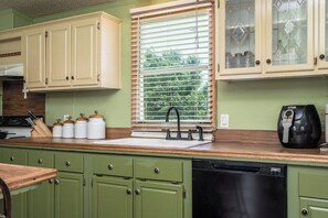 A kitchen with green cabinets, a window with blinds, a coffee maker, and a dishwasher.