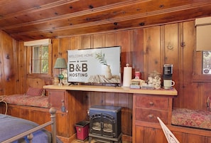 Een houten hut binnen met een bed, een bank, een open haard, een bordje met de tekst 'Welcome Home B&B Hosting' en een koffiezetapparaat.