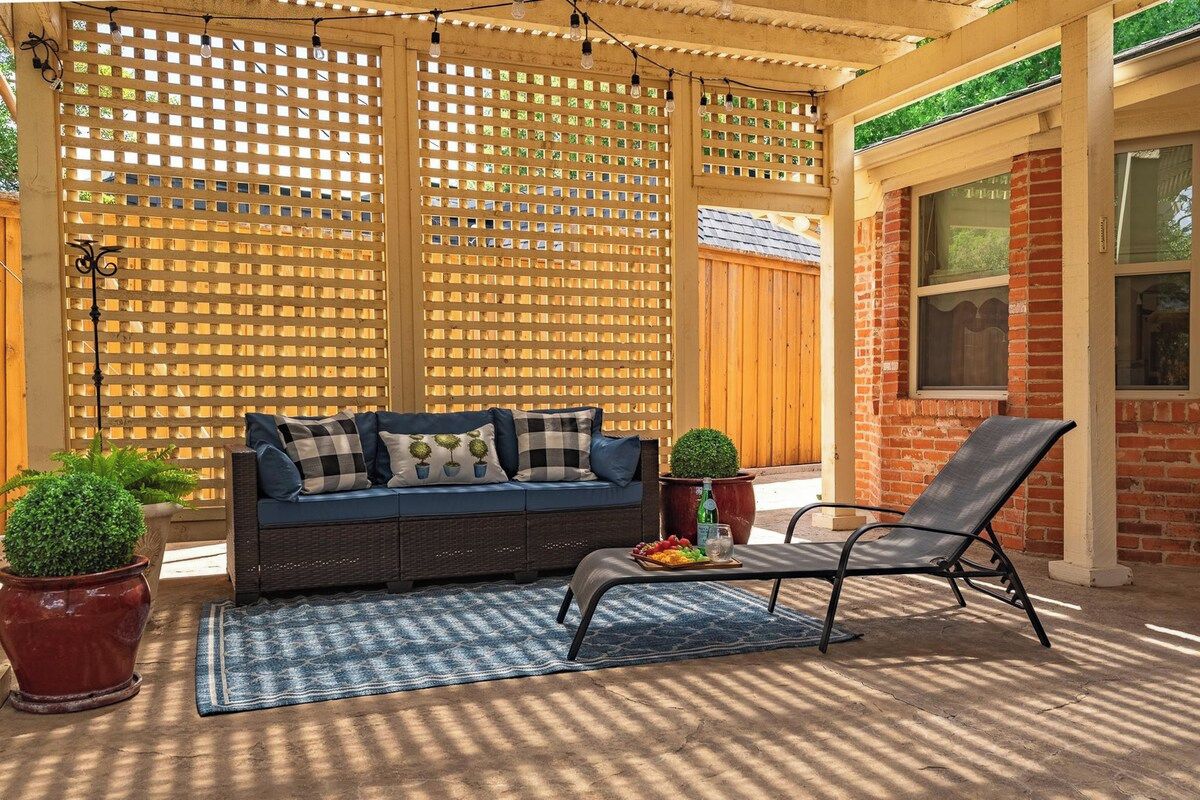 A covered patio area with a sofa and a lounge chair, a wooden lattice fence, and potted plants.