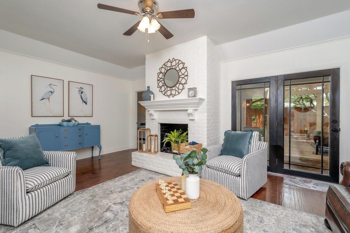 A living room with a fireplace, striped sofas, a coffee table with a chess set, and a ceiling fan.