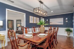 A dining room with a wooden table set for eight, surrounded by matching chairs. - The Blue Bonnet – Charming 3-Bedroom Coastal (Abilene)