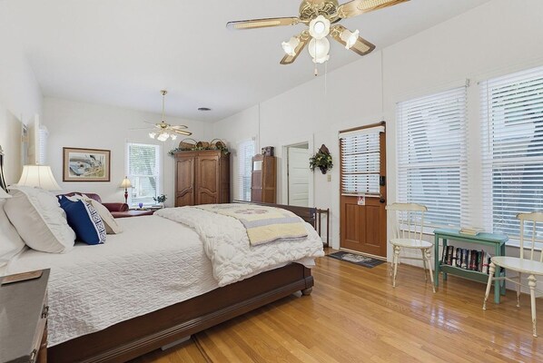 A bedroom with a bed, a ceiling fan, a wooden wardrobe, and a window with blinds.