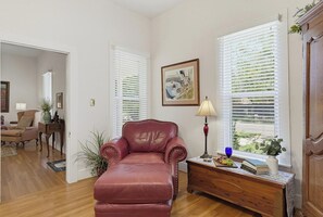 Een woonkamer met een leren fauteuil, een houten bijzettafeltje met boeken en een lamp, en een schilderij aan de muur.