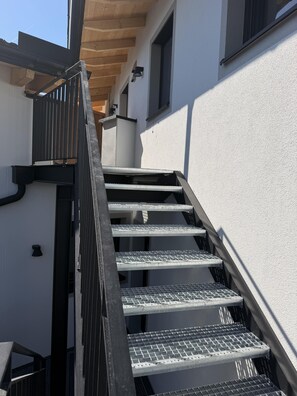 A metal staircase with a handrail leading to a landing, adjacent to a white wall with a window. - Limone Apartment with Rooftop Terrace (Bernau am Chiemsee)