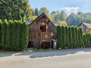 A rustic wooden cabin with a porch, surrounded by neatly trimmed evergreen trees.