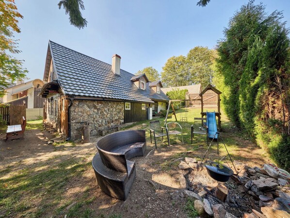A rustic house with a stone exterior, a tiled roof, and a wooden deck.