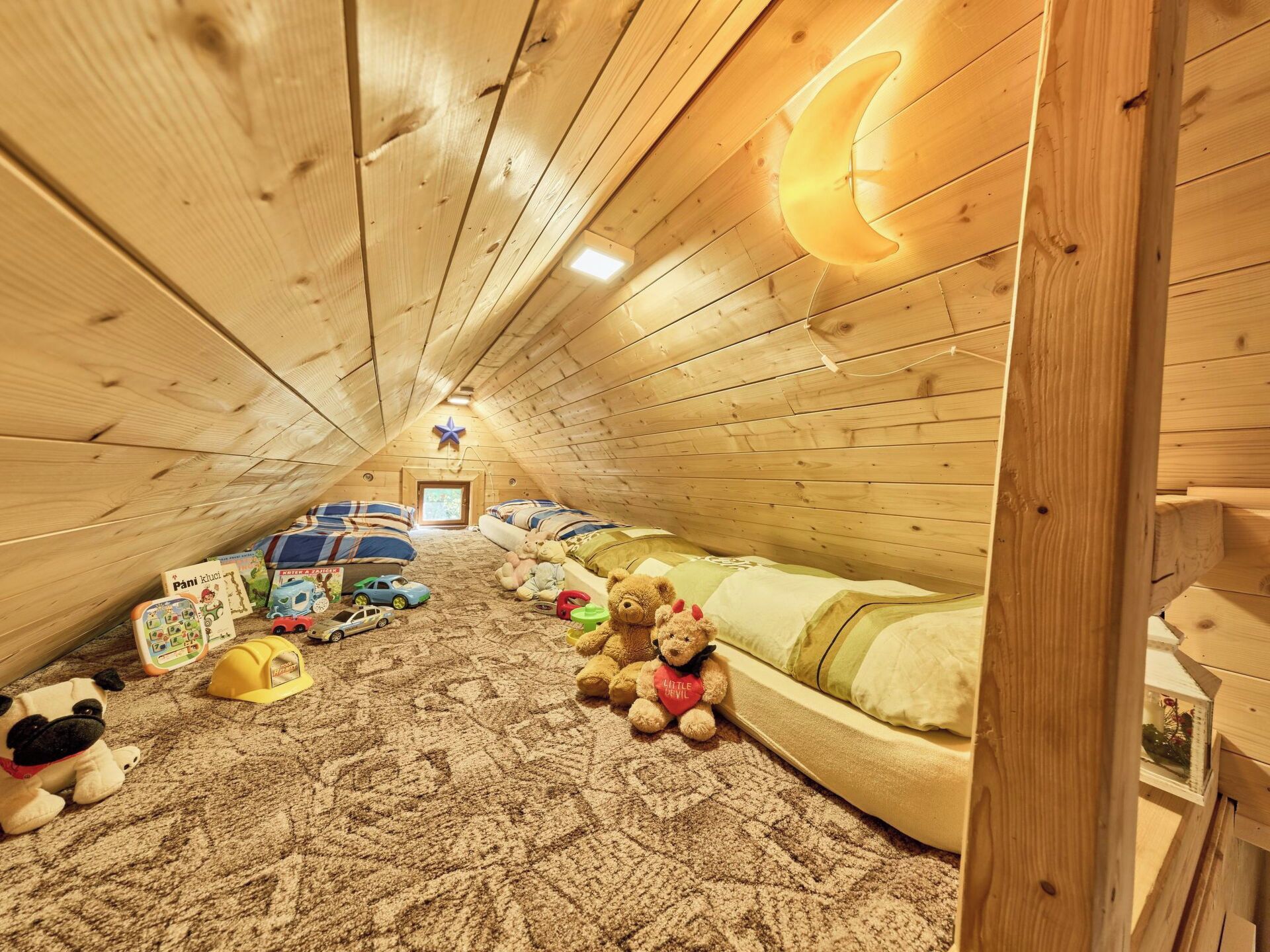 A cozy attic bedroom with a sloped ceiling, wooden walls, a bed with a crescent moon light, and various children's toys and books.