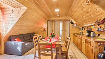 Un intérieur chaleureux en bois, comprenant un coin repas, un canapé et une petite cuisine.