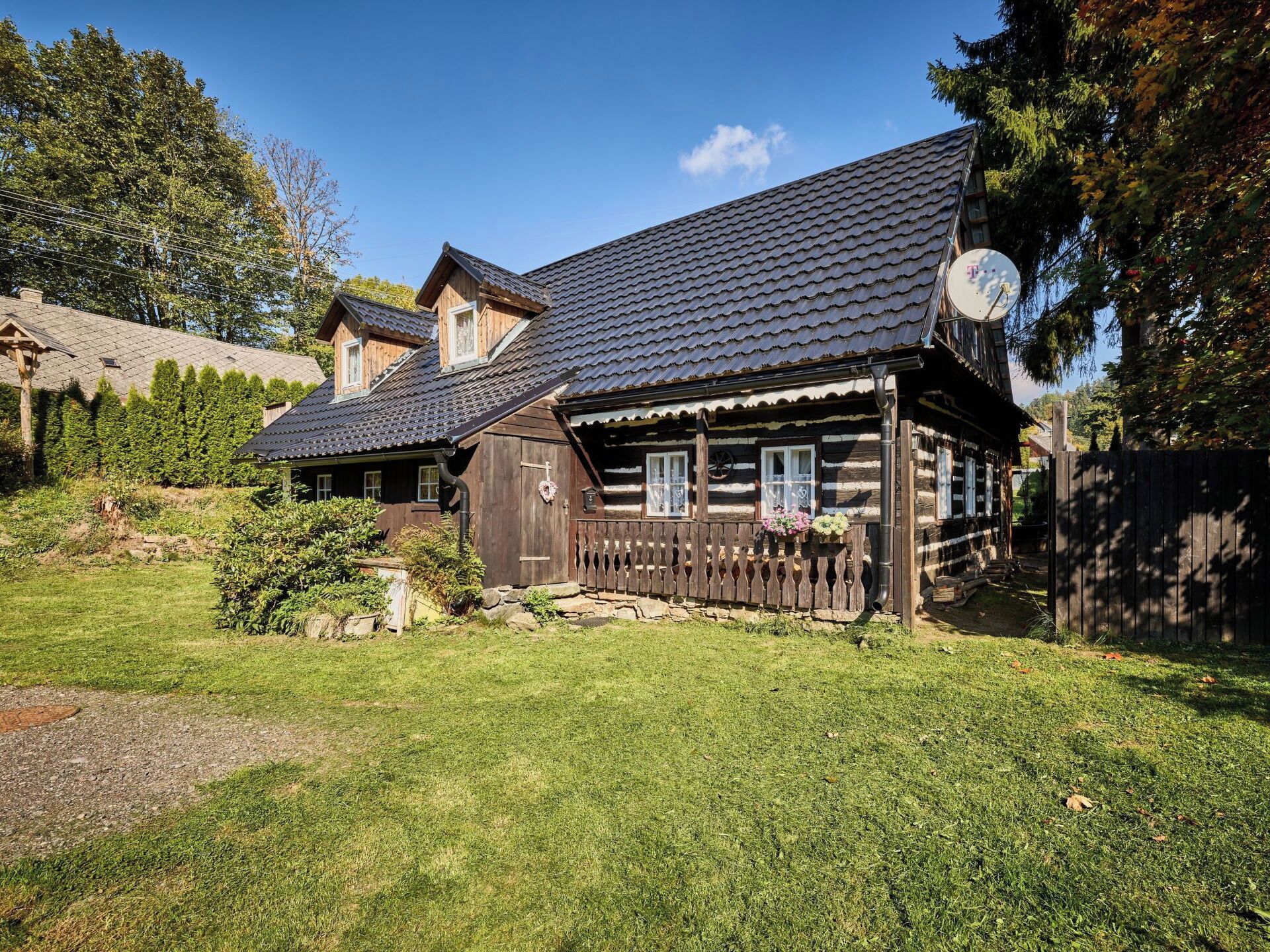A wooden cabin with a sloped roof, a satellite dish, and a fenced yard.