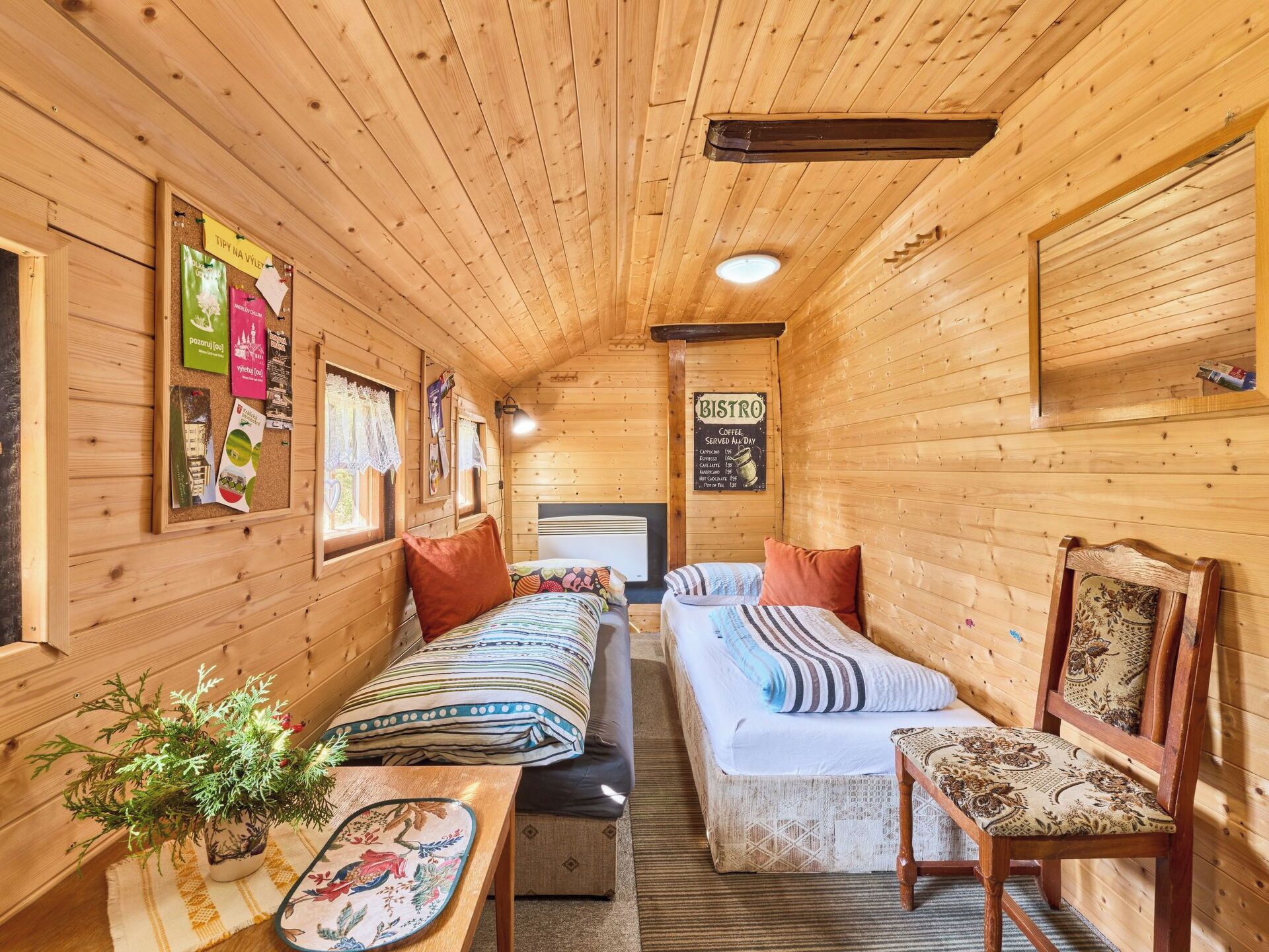 Interior acogedor de una cabaña de madera con una cama, una mesa con una planta y un cartel que indica un bistro que sirve café.