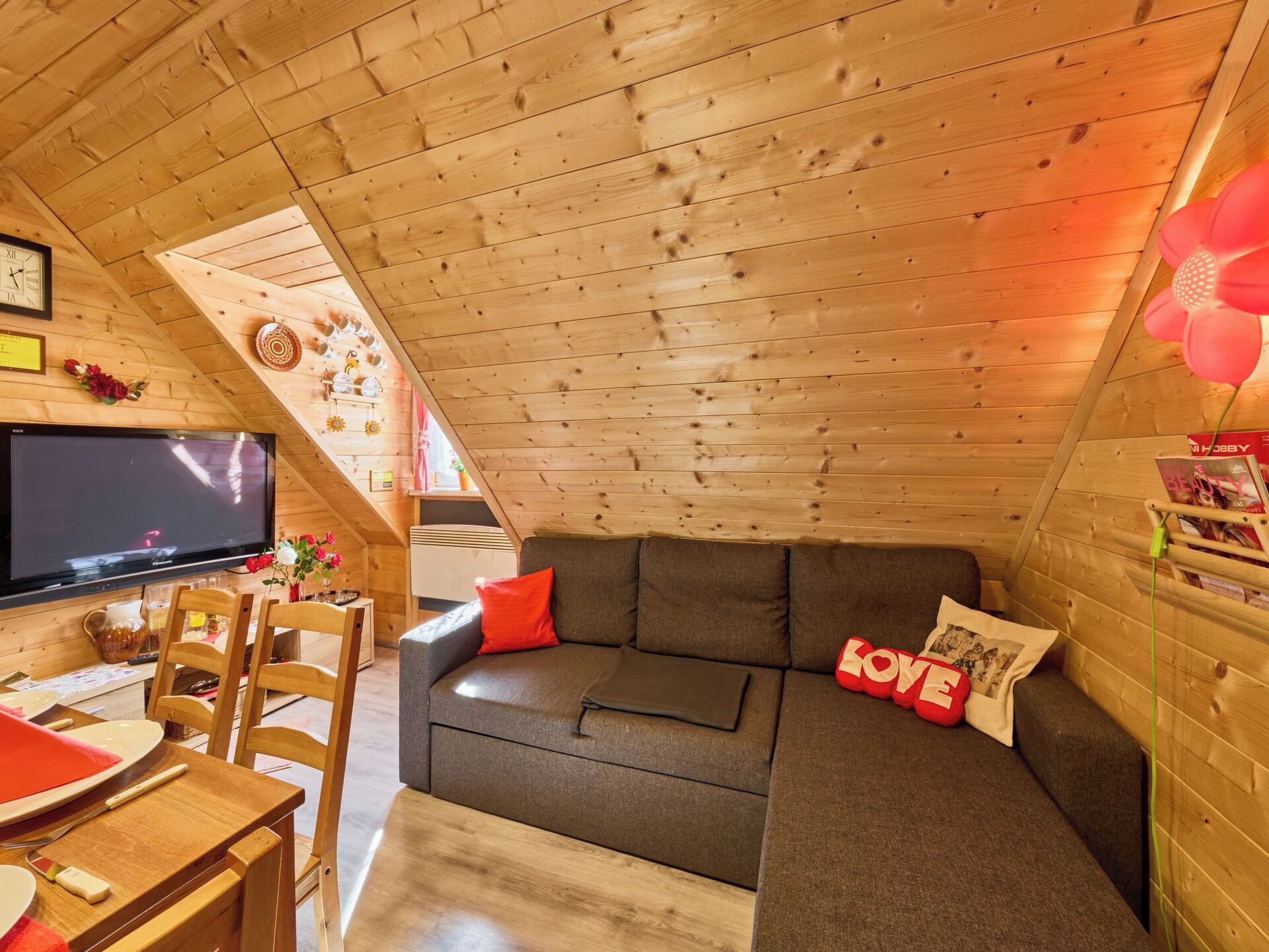 Une pièce confortable de style loft, avec un plafond en bois, un canapé gris, une table à manger avec des chaises et un téléviseur à écran plat.