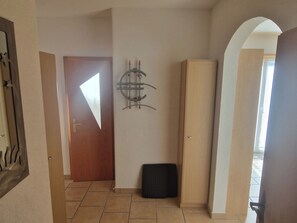 A hallway with a wooden door, a black trash bin, and a wooden cabinet. - Birke, (Grächen), by Interhome (Grächen)