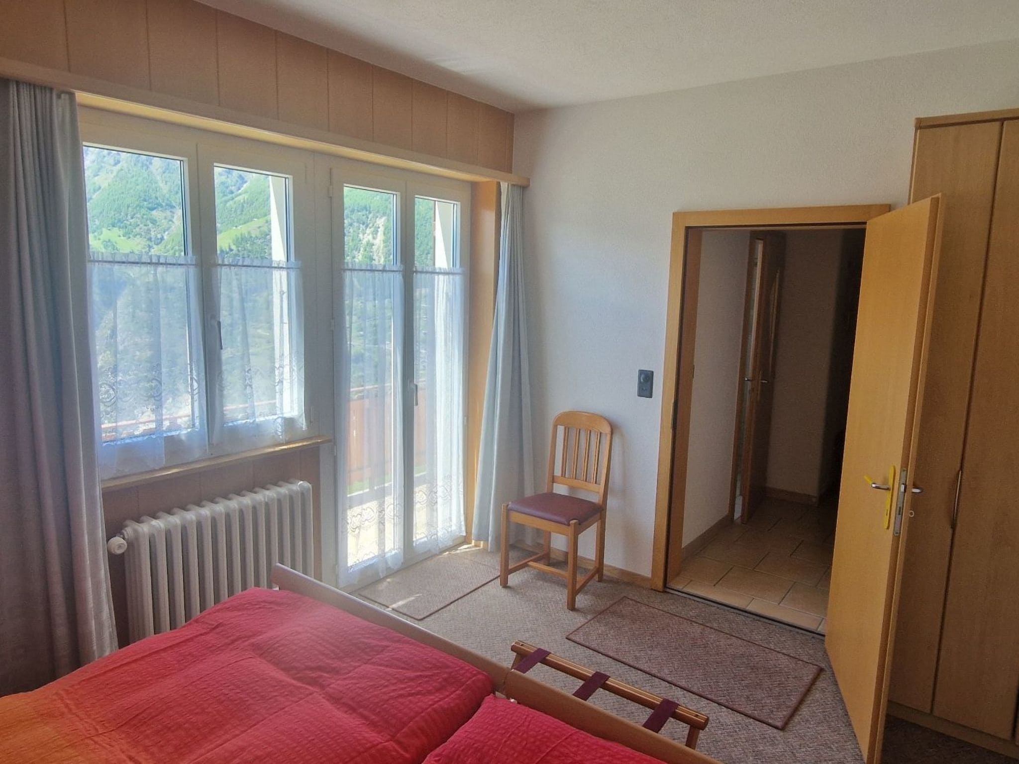 A bedroom with a bed, a chair, a radiator, and a door leading to another room.