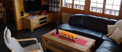 Una sala de estar con un sofá de cuero negro, una mesa de centro de madera y un televisor sobre un mueble de madera.