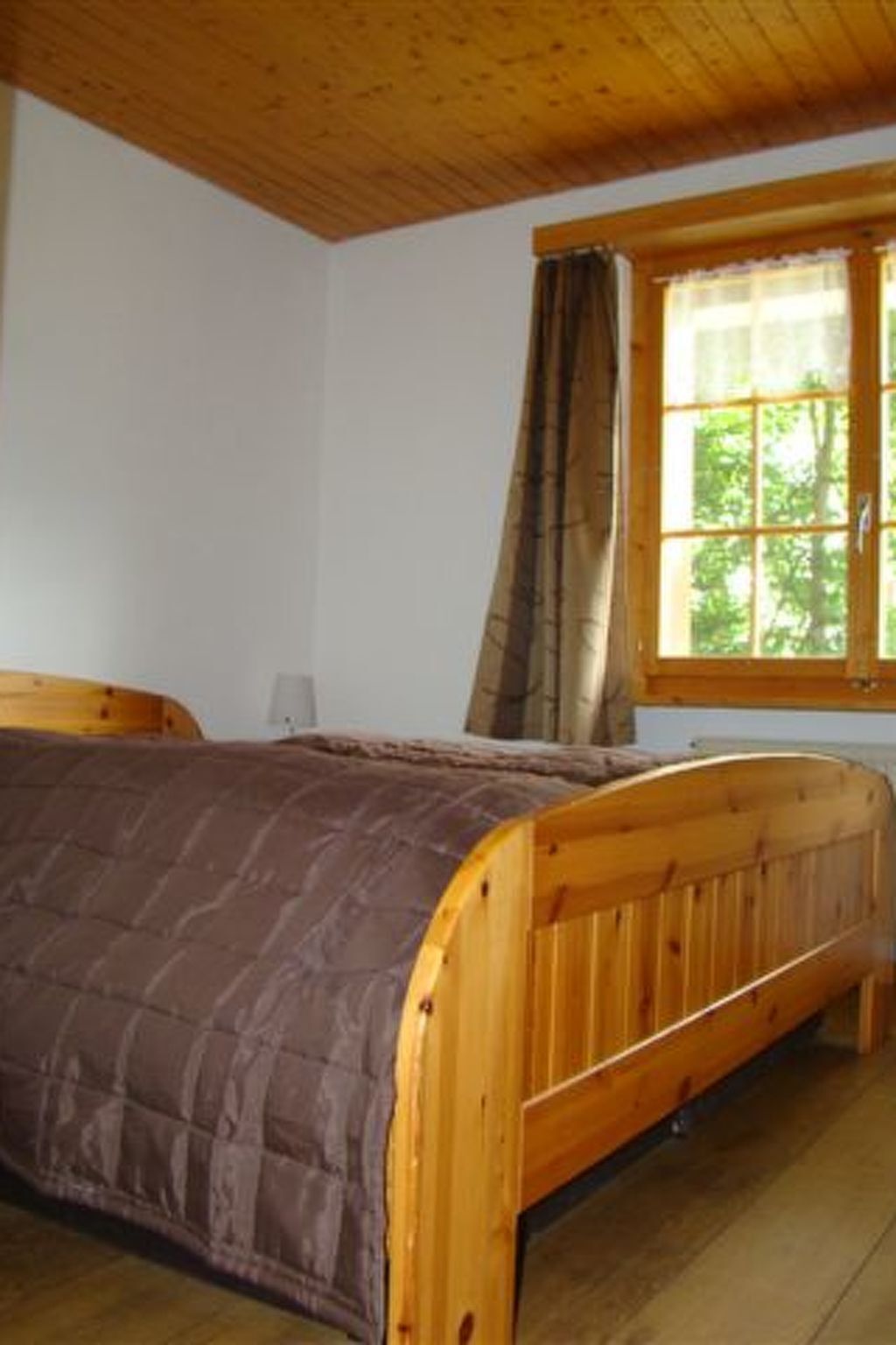 A room with a wooden bed, a window with curtains, and a white wall.