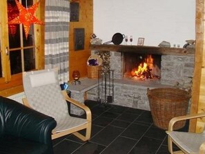 Ein gemütliches Zimmer mit Kamin, Holztisch und bequemen Sessel.