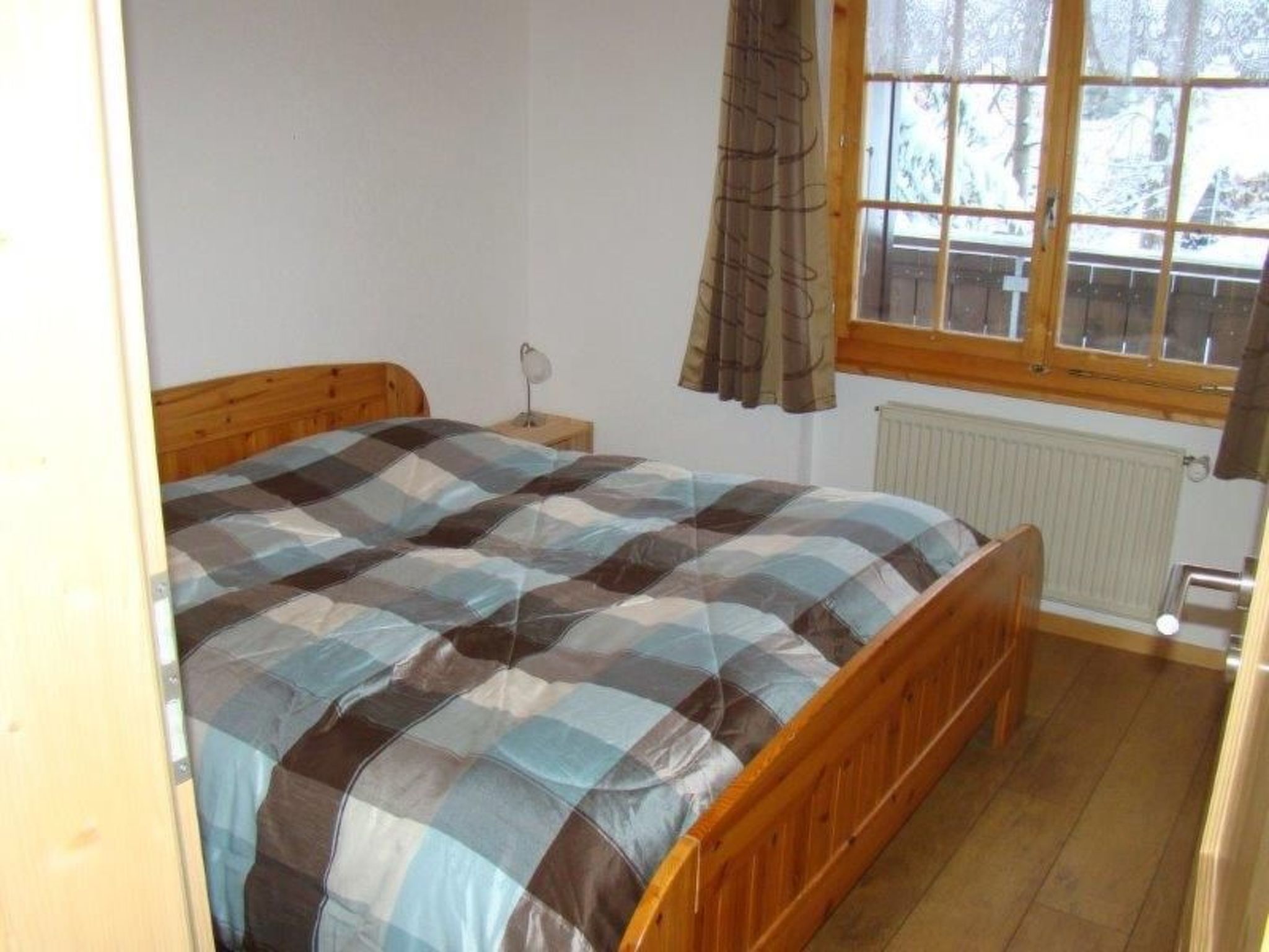 A bedroom with a wooden bed, a nightstand, a window with curtains, and a radiator.