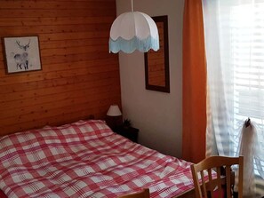 A room with a wooden wall, a bed with a checkered bedspread, a hanging lamp, a framed picture, and a window with curtains. - David 26D, (Grächen), 1623 by Interhome (Grächen)